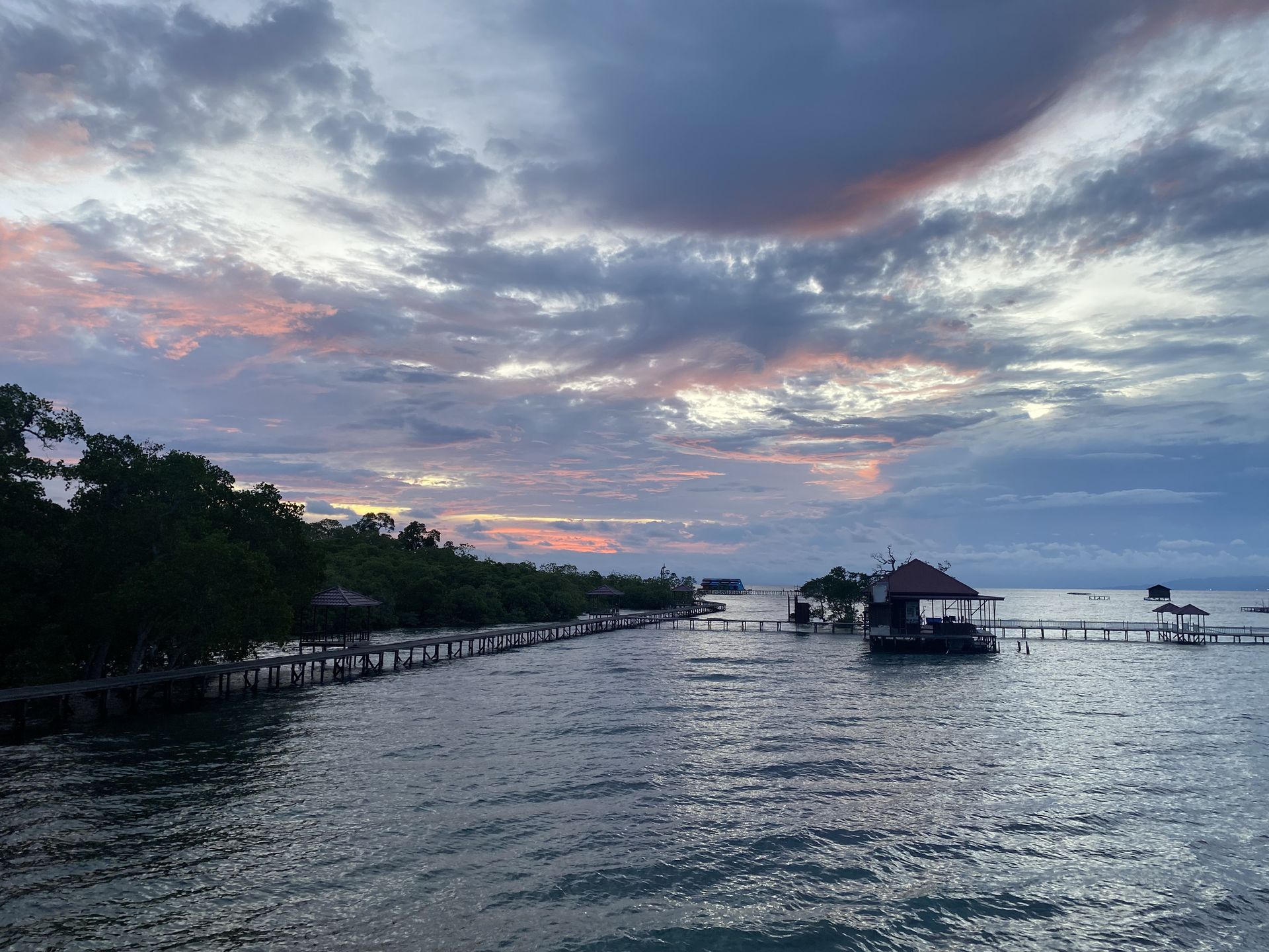 Sore hari di Pulau Miang menghadirkan pemandangan yang menenangkan, dengan matahari terbenam di cakrawala, laut tenang, dan aktivitas nelayan yang masih terlihat di teluk.